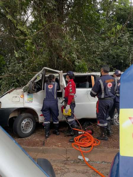 Equipe de resgate trabalhando em um veículo acidentado perto de árvores.