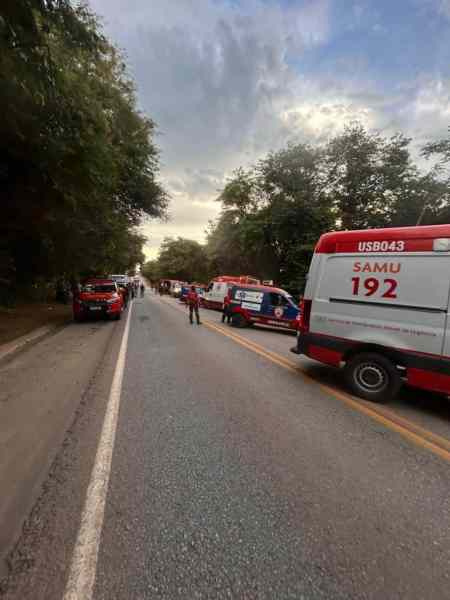 Caminho com várias ambulâncias do SAMU 192 estacionadas ao lado, com pessoas próximas em um ambiente arborizado.