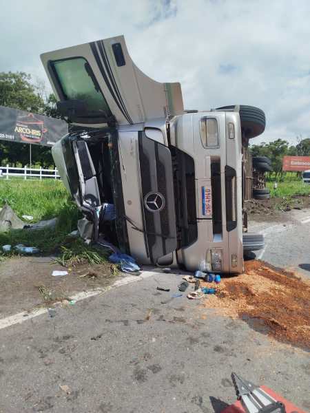 Caminhão acidentado de lado na estrada, com danos visíveis e detritos ao redor.