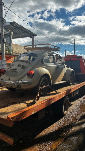Um carro Fusca antigo sendo transportado em uma carreta, com céu nublado ao fundo.