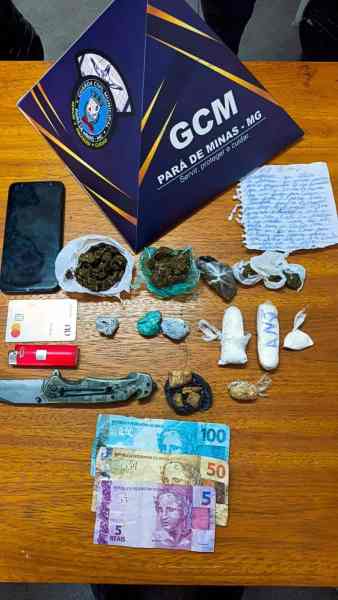 Objetos apreendidos incluindo drogas, dinheiro em notas de diferentes valores, um celular e uma faca, dispostos sobre uma mesa.