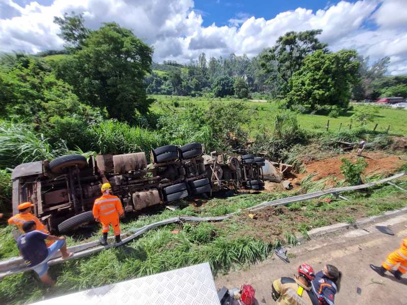 Um caminhão tombado ao lado da estrada com várias pessoas trabalhando na recuperação, em uma área verdejante.