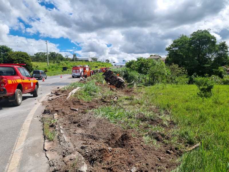 Acidente de carro na estrada, com veículo capotado na margem e viaturas de emergência presentes.