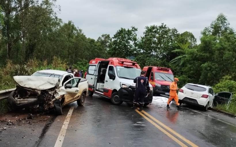 Accidente de carro em estrada com veículos danificados e ambulâncias presentes. Equipe de resgate em ação.