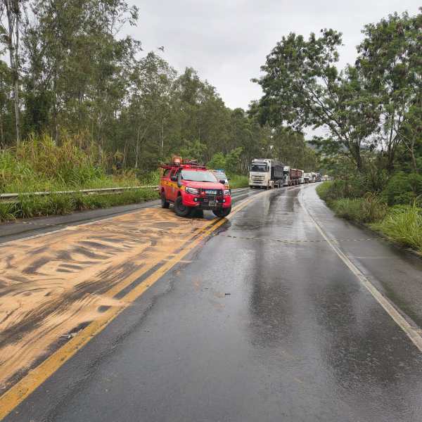 Veículo de bombeiros estacionado ao lado da estrada com pista escorregadia, ao fundo há uma fila de caminhões.