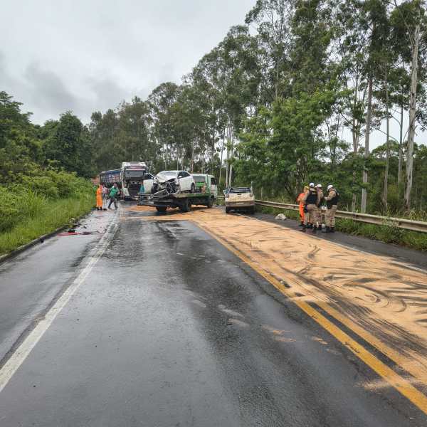 Acidente de carro em estrada molhada, com veículos danificados e equipes de emergência trabalhando na limpeza do local.