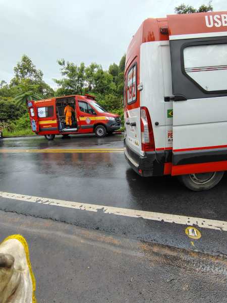 Ambulâncias estacionadas em uma estrada molhada, com um socorrista vestido de laranja saindo de uma delas.