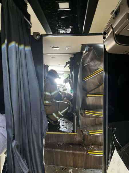 Interior de um ônibus danificado, com um bombeiro sentado entre as cadeiras e a escada destroçada visível ao fundo.