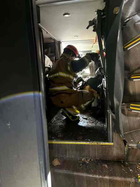 Bombeiro em uniforme de proteção analisando os danos dentro de um veículo, com sujeira e detritos ao redor.