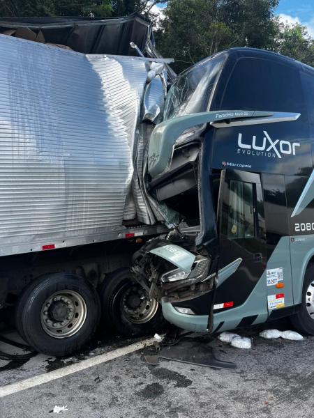 Ônibus Luxor com colisão frontal em caminhão, com danos visíveis na cabine do ônibus e no reboque.