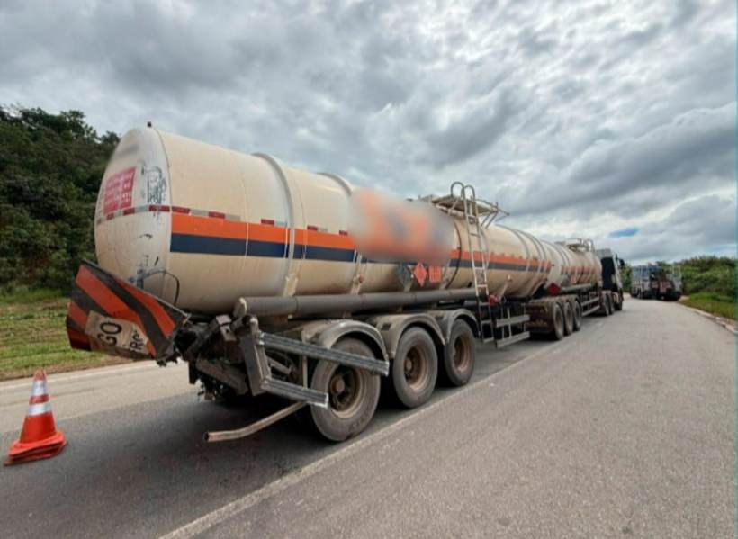 Caminhão tanque parado na estrada com nuvens ao fundo e cones de sinalização.
