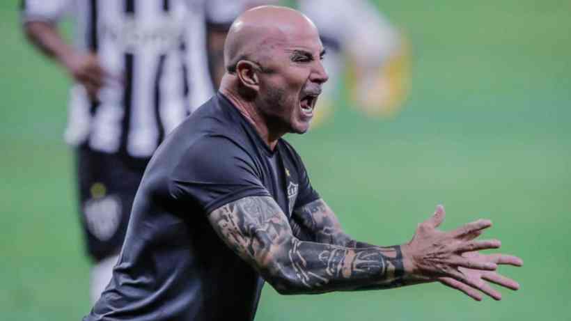 A coach passionately gesturing and shouting on the sidelines during a soccer match.