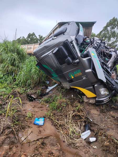 Caminhão acidentado em uma área coberta de grama e lama, com a cabine inclinada para o lado.