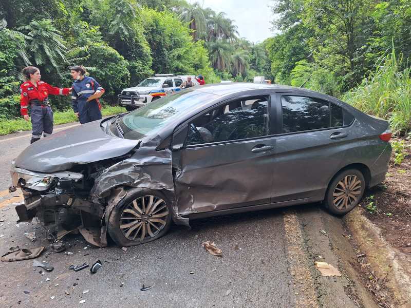 Carro acidentado na estrada, com a lateral danificada, enquanto socorristas atendem a situação nas proximidades.