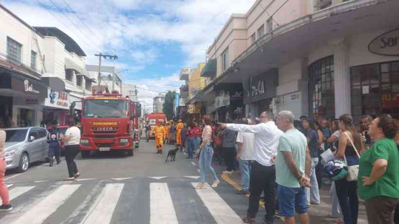 Cruzamento urbano com um caminhão de bombeiros e pessoas observando, algumas vestindo uniformes de emergência, em uma rua comercial movimentada.