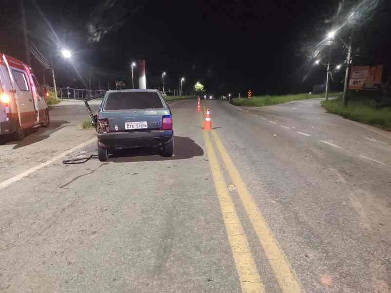 Carro estacionado em uma estrada à noite, com lanternas acesas e cones de sinalização ao redor.