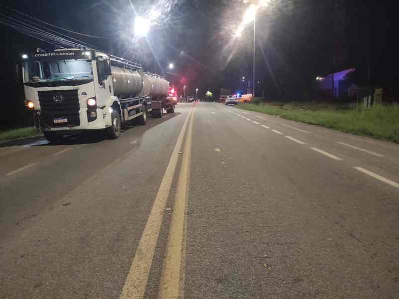 Caminhão tanque estacionado em uma estrada durante a noite, iluminada por postes de luz.