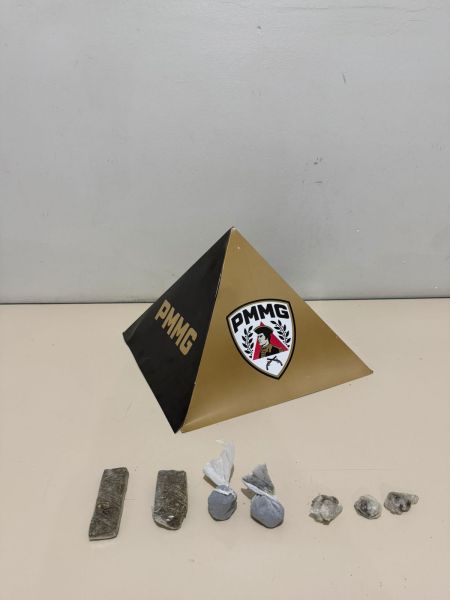 Pirâmide com logo da PMMG e quatro objetos em exposição à frente, incluindo dois tijolos e pedras.