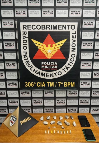 Mesa com objetos apreendidos, incluindo pedras brancas e dois dispositivos móveis, atrás de um banner da Polícia Militar de Minas Gerais.
