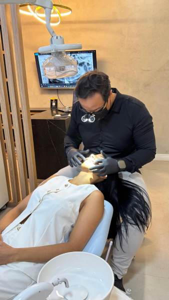 Um dentista realizando um procedimento dental em uma paciente em um consultório moderno, com um monitor ao fundo exibindo imagens relacionadas ao tratamento.