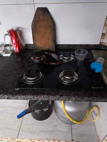 Fogão a gás com quatro bocas, panela sobre a mesa, garrafa de vidro e utensílios ao fundo.