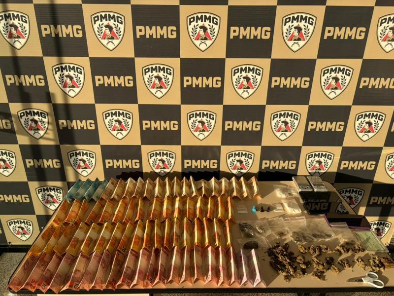 Mesa com pacotes de substâncias, organizados em fileiras, em frente a um fundo com logo da PMMG.