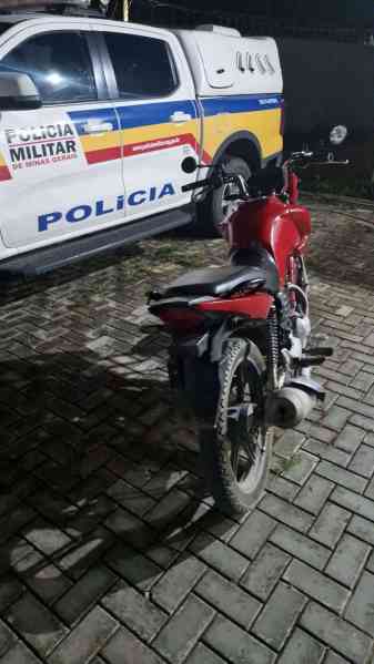 Uma motocicleta vermelha estacionada ao lado de uma viatura da Polícia Militar de Minas Gerais durante a noite.
