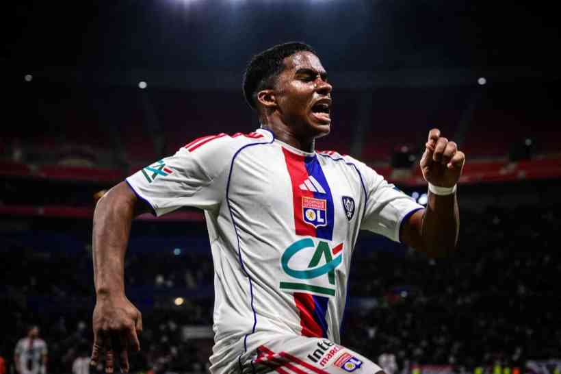 A soccer player celebrating passionately after scoring a goal, wearing a white jersey with red and blue accents.