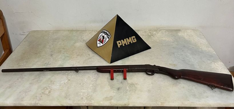 Rifle de madeira em uma mesa ao lado de um símbolo em forma de pirâmide da PMMG.