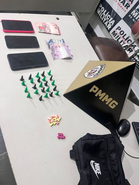 Mesa com objetos apreendidos, incluindo três celulares, cédulas de dinheiro, e diversas embalagens de substâncias aparentando serem drogas, além de uma mochila preta da marca Nike.