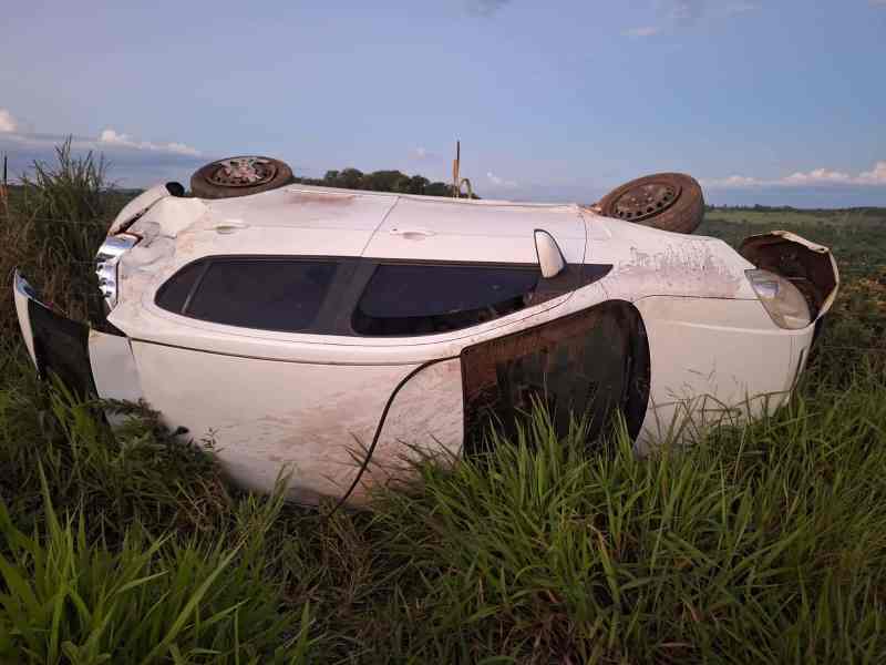 Carro branco capotado em meio à grama alta.