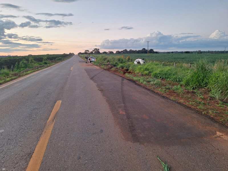 Estrada rural com vegetação ao redor, céu estrelado e um veículo parado à margem.