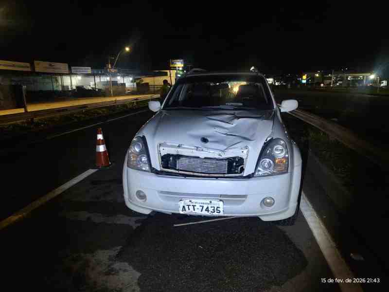 Veículo branco danificado com capô quebrado em uma estrada à noite.