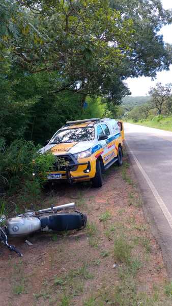 Veículo de polícia parado na beira da estrada, próximo a uma motocicleta tombada.