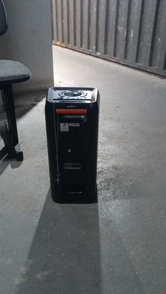 Um aquecedor portátil preto em um espaço interno com piso de concreto.