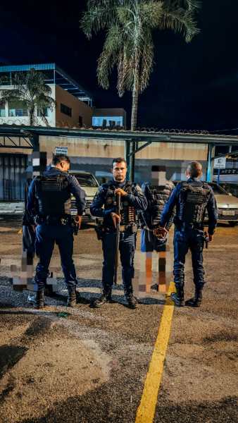 Policiais em uma rua à noite, armados e com coletes à prova de balas, observando a situação enquanto estão em grupo.