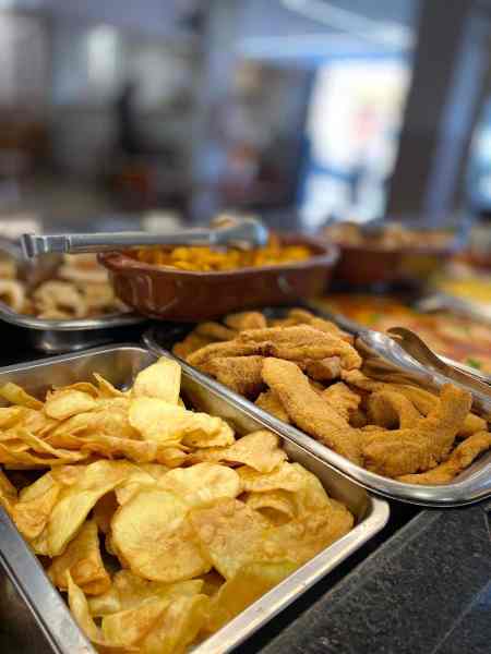 Prato com batatas fritas crocantes e tiras de frango empanadas em uma mesa de buffet.