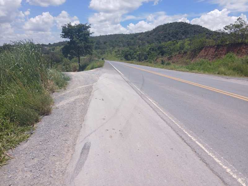 Estrada com vegetação ao lado, montanhas ao fundo e céu parcialmente nublado.