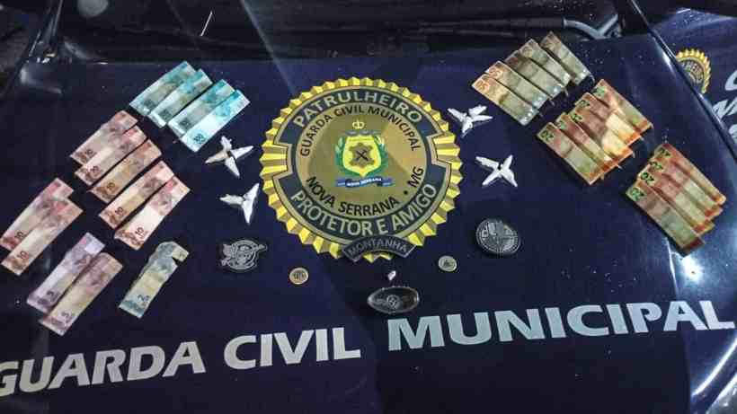 Dinheiro em notas e objetos sobre o capô de um carro da Guarda Civil Municipal.