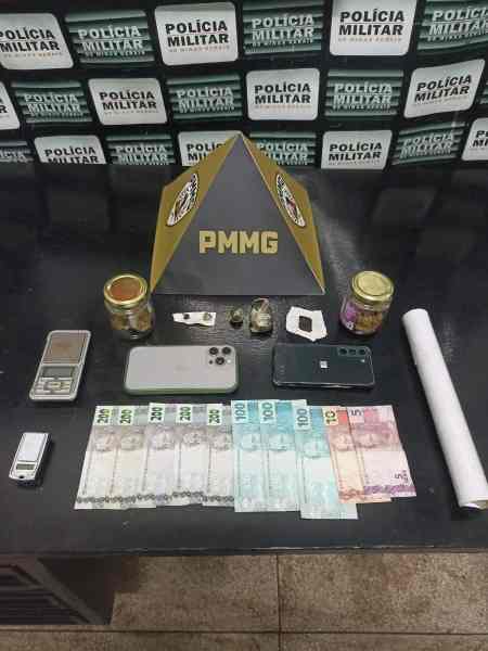 Imagem de itens apreendidos pela polícia, incluindo dinheiro em notas, celulares, balança, frascos e uma pirâmide com a sigla PMMG ao fundo.