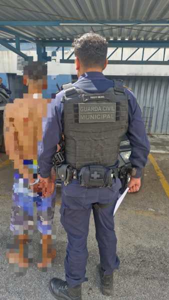 Policial da Guarda Civil Municipal abordando um homem detido em local externo.