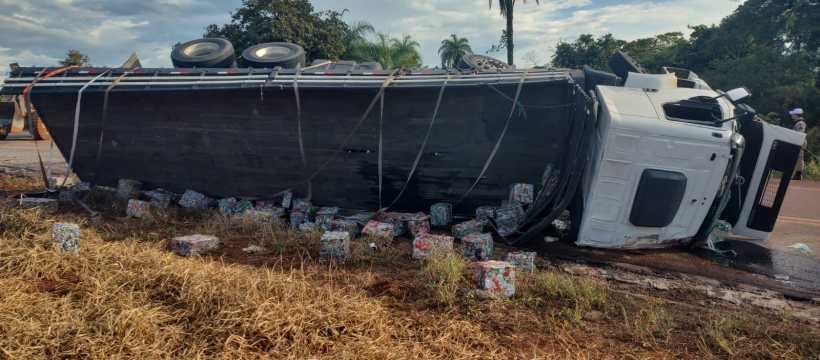 Caminhão tombado na estrada, com cargas espalhadas pelo chão e vegetação ao redor.