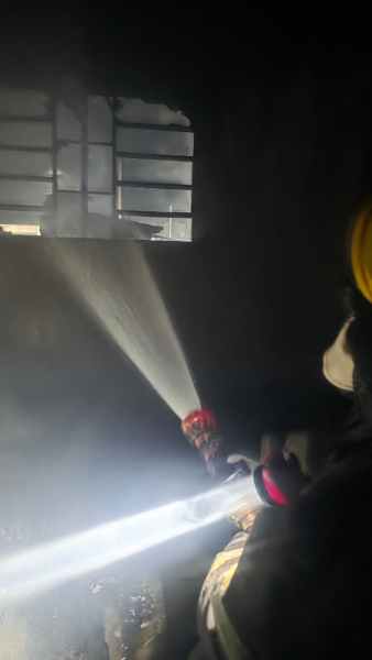Bombeiro usando uma mangueira de incêndio em um ambiente escuro, com luz intensa visível.