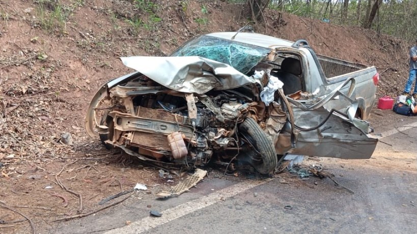 Carro acidentado com danos significativos na lateral e frente, localizado em uma estrada em área rural.