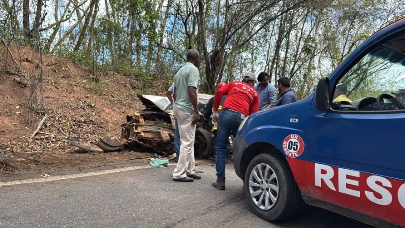 Um acidente de carro na estrada, com um veículo danificado ao lado da pista e várias pessoas prestando assistência.