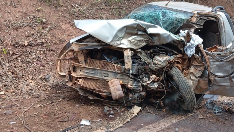 Veículo capotado e danificado em um acidente de trânsito, com partes expostas do motor e uma roda visível.