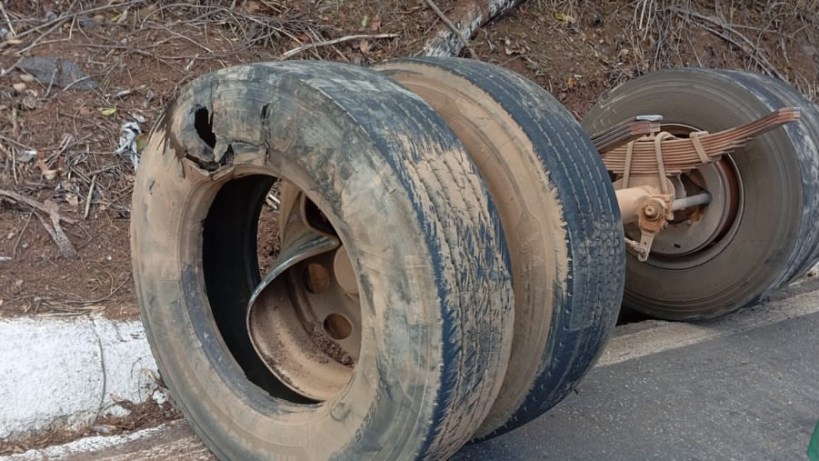 Pneu danificado abandonado à beira da estrada, com marcas de desgaste visíveis e sujeira acumulada.