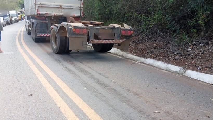 Caminhão estacionado em uma estrada, com marcas de pneus visíveis na pista e vegetação ao fundo.